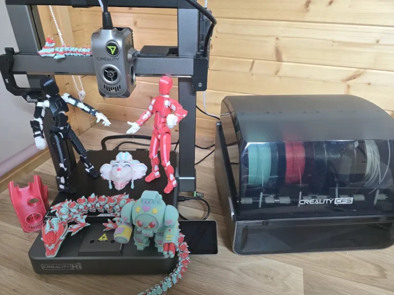 Creality Hi Combo 3D printer beside completed multi-color prints and a CFS filament storage box demonstrating an additive manufacturing workflow.