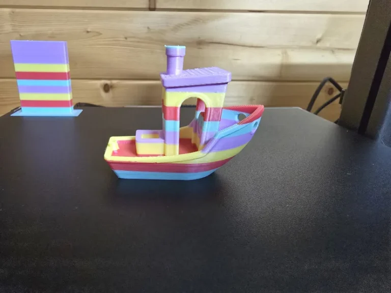 Rainbow-striped 3D Benchy boat printed with multi-color filament on a Creality Hi Combo 3D printer.