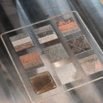 Close-up of a metal substrate with nine distinct multi-metal 3D printed alloy patches demonstrating graded compositions in metal additive manufacturing